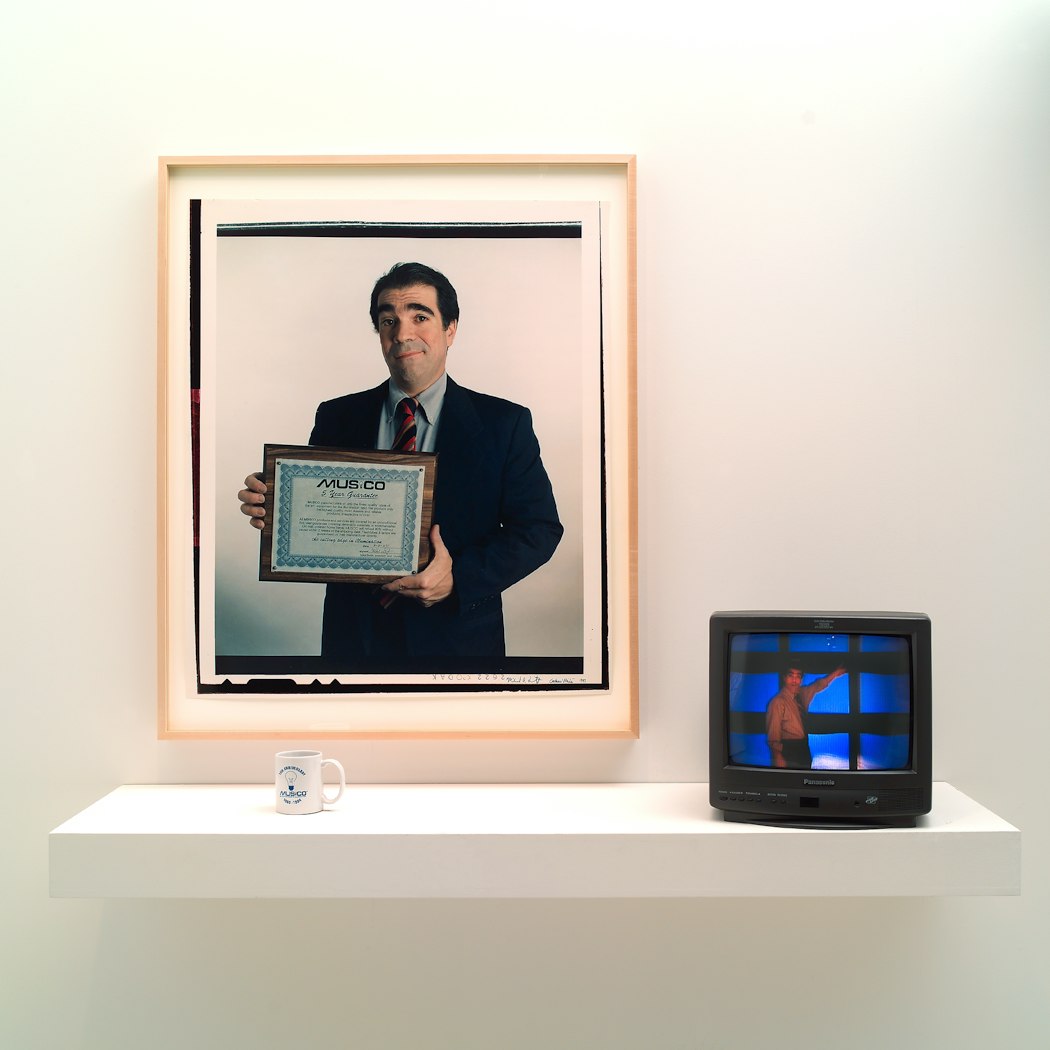 video still shows man in front of wall of video monitors